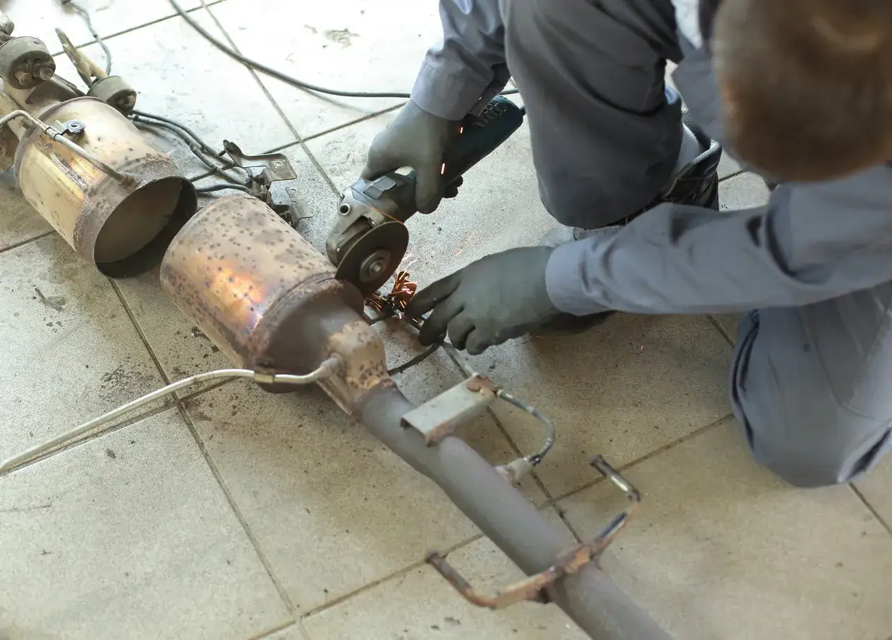 Mechanik przecina szlifierką element układu wydechowego, prawdopodobnie GPF. Iskry sypią się podczas pracy.