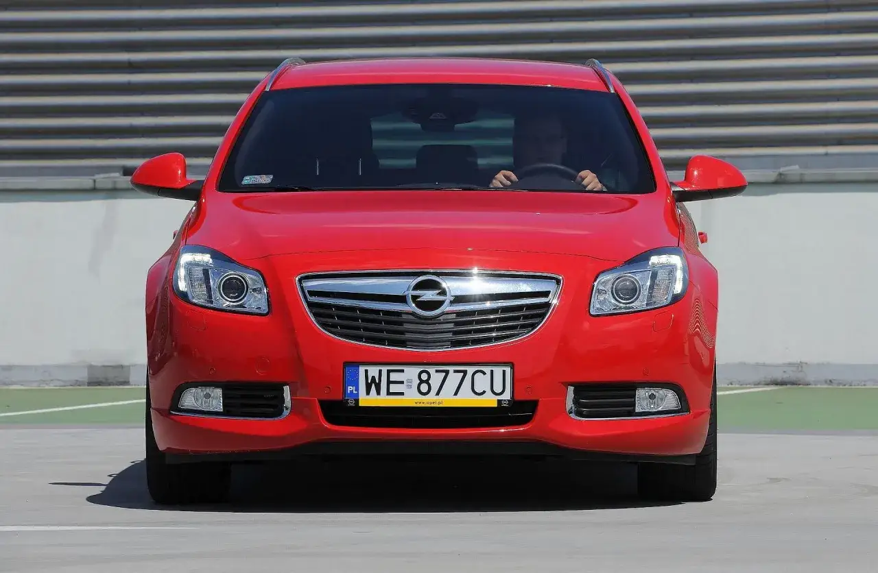 Czerwony Opel Insignia 2.0 CDTI z polskimi tablicami WE 877CU na tle szarego muru.