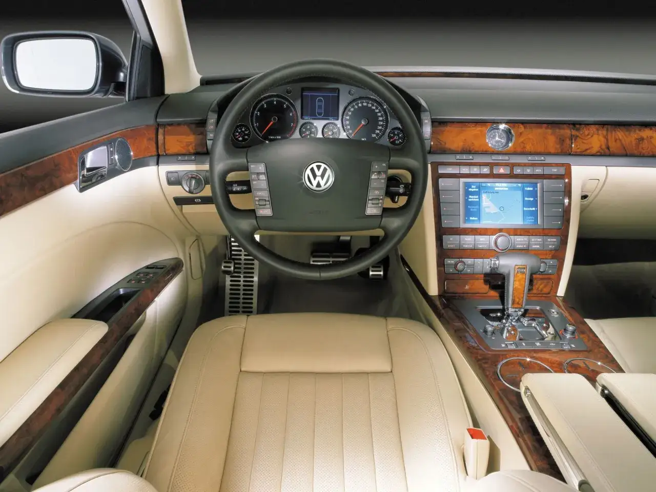 Wnętrze luksusowego VW Phaeton z beżową skórzaną tapicerką, drewnianymi wstawkami i nowoczesnym panelem multimedialnym.