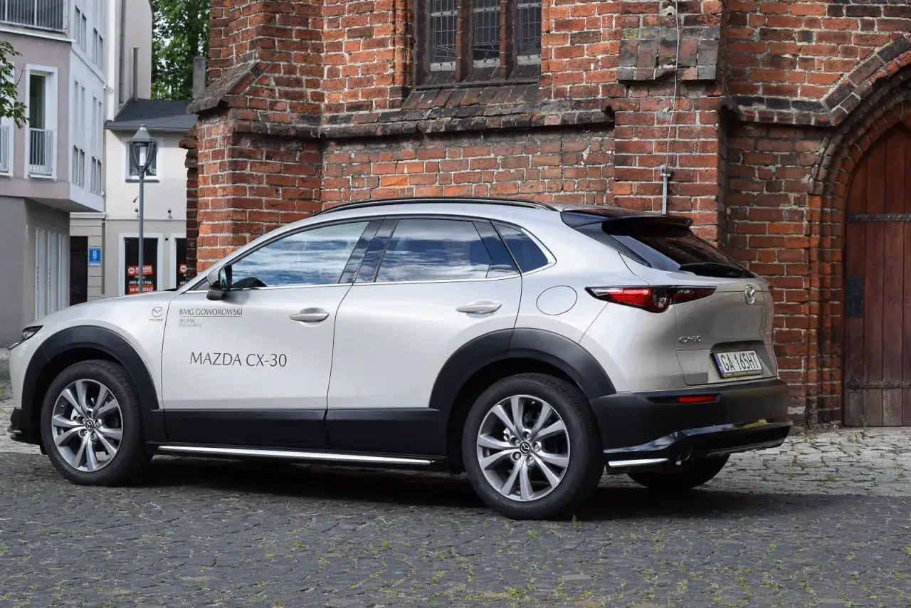 Srebrna Mazda CX-30 na brukowanej ulicy. Zwróć uwagę na jej kompaktowe mazda cx 30 wymiary, idealne do miasta.