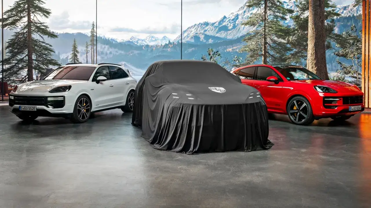 Białe i czerwone Porsche Cayenne stoją obok siebie. Centralnie umieszczony, przykryty czarnym pokrowcem model sugeruje tajemnicę i pytanie: ile kosztuje Porsche?