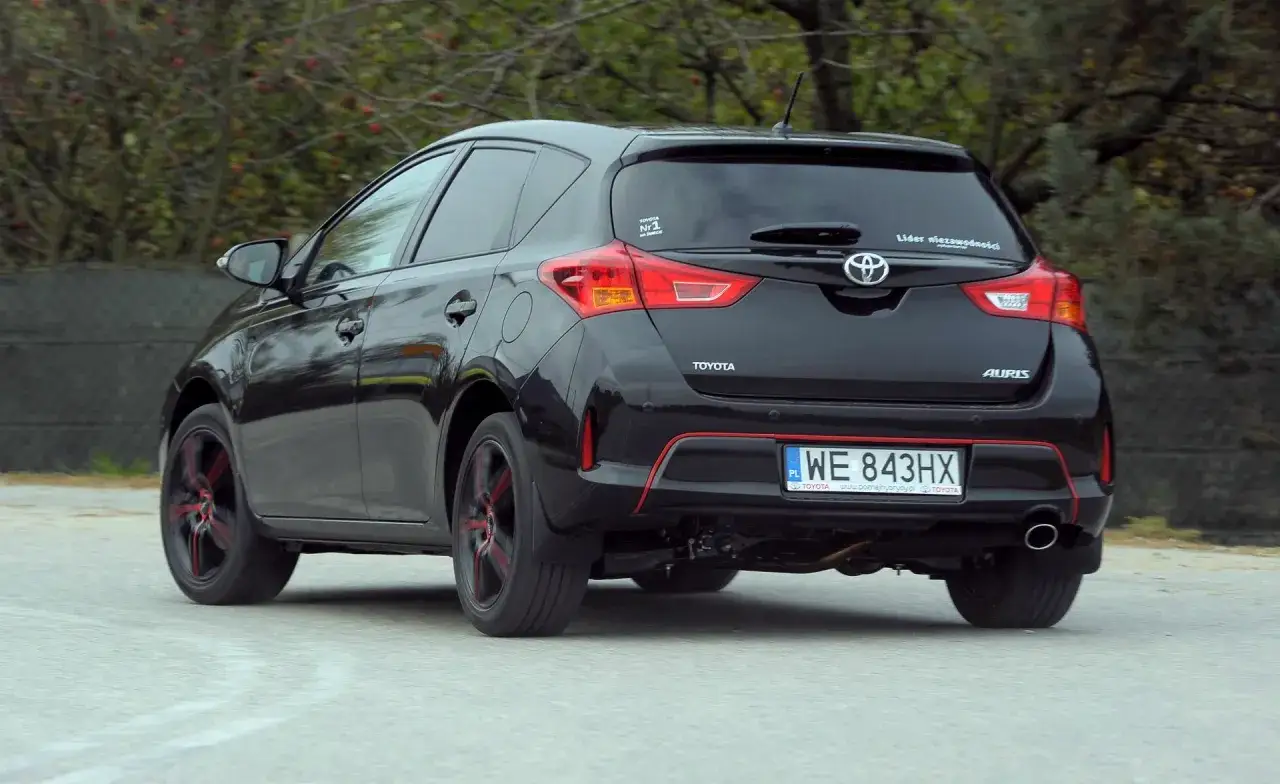 Czarny Toyota Auris 1.6 benzyna z czerwonymi akcentami na felgach i zderzaku, jadący po drodze.