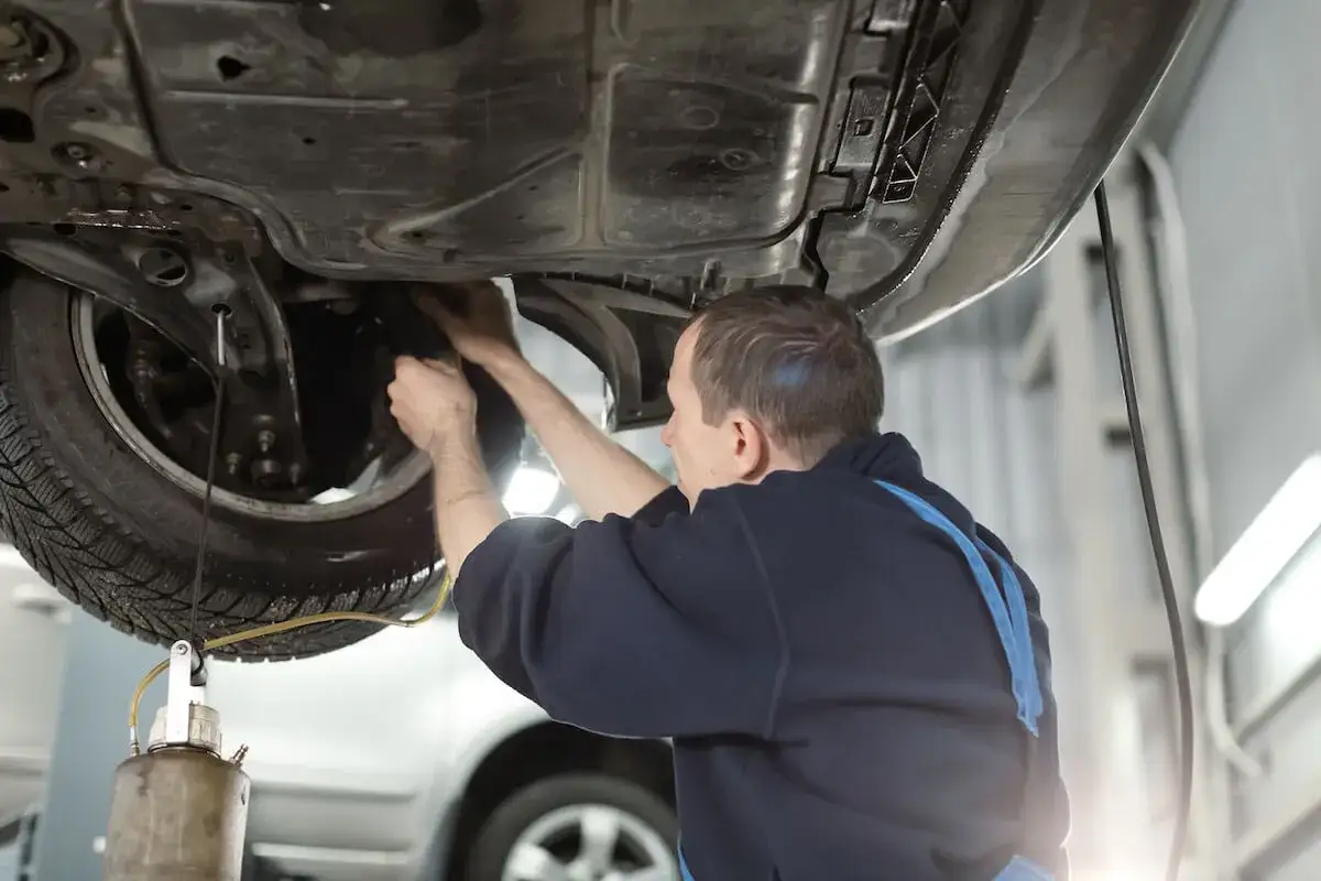 Mechanik dokonuje wymiany płynu hamulcowego, pracując pod podniesionym samochodem.